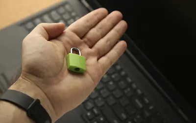 Mano sosteniendo un candado verde sobre un portátil