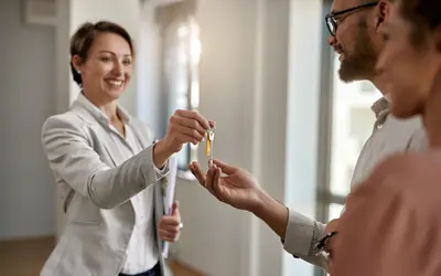 A woman hands over the keys of a home to a couple
