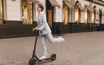 Mujer sonriente en patinete eléctrico por una calle peatonal